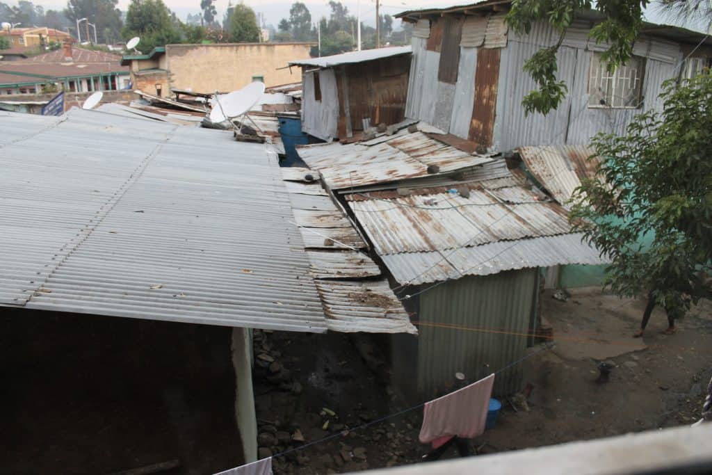 Rundown metal rooftops in an impoverished neighborhood, showing signs of rust and damage, with satellite dishes and hanging laundry, highlighting the importance of safety education for children.
