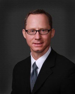 Portrait of a professional man wearing glasses in a black suit, promoting children's safety and the "Don't Stick Don't Stuff" book.