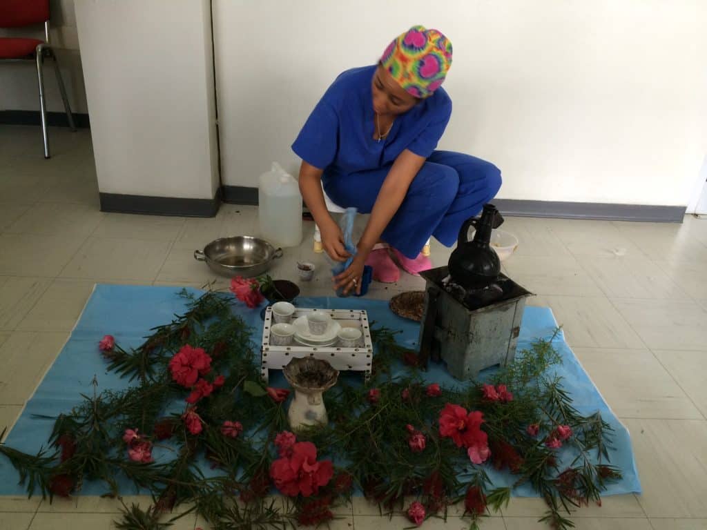 Cute woman in blue scrubs with rainbow-colored cap, teaches kids safety using a traditional fire safety demonstration with flowers and household items.
