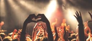 Vibrant concert scene with hands raised, including a person forming a heart shape, capturing lively music event emphasizing fun, safety, and engagement for kids and families.